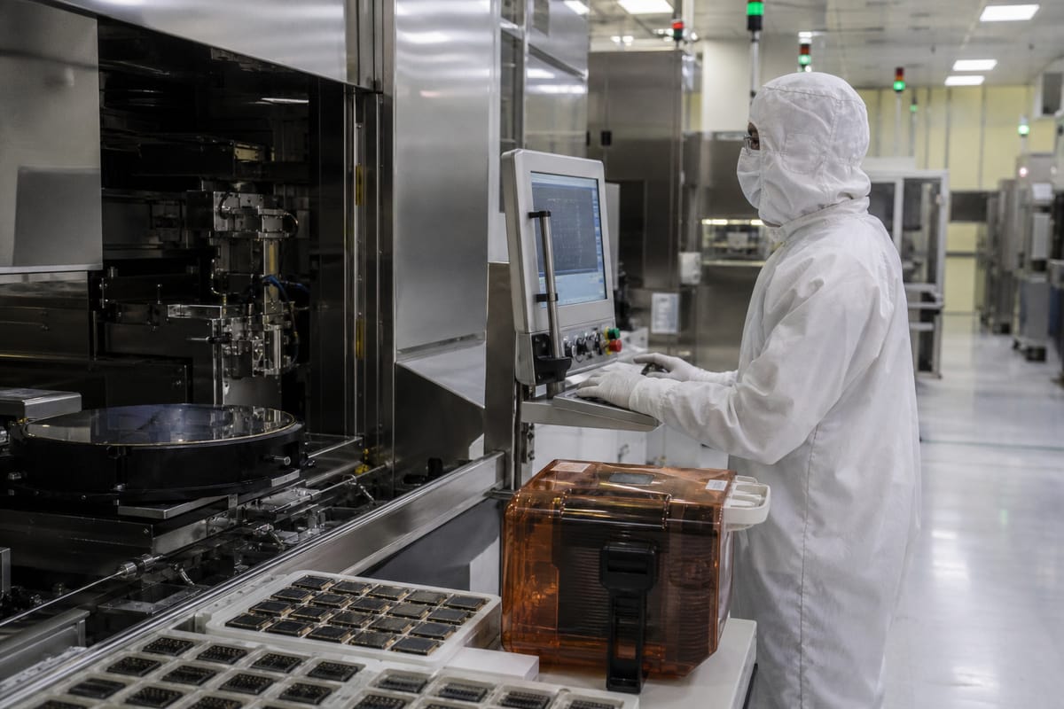 Photoreal documentary close-up of an advanced semiconductor packaging line with a cleanroom technician inspecting large accelerator packages surrounded by high-bandwidth-memory stacks on a 300-millimetre wafer-handling station.